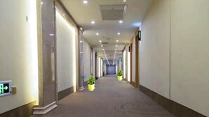 A long, well-lit hallway with a patterned carpet, potted plants, and a visible exit sign. - GreenTree Inn Hefei Feixi County South Jinzhai Road Jinyun International Hotel (Hefei)