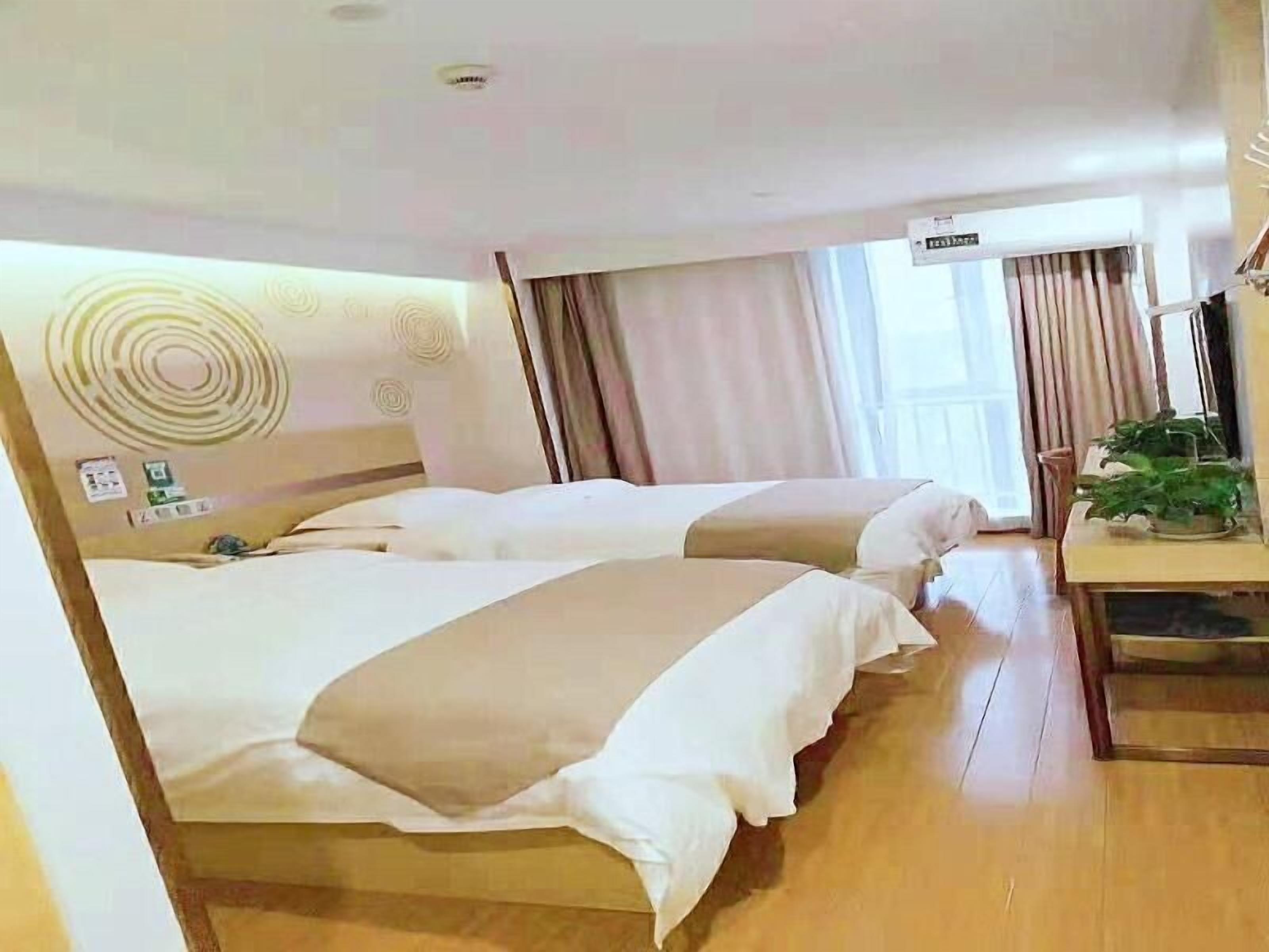 A hotel room with two beds, a wooden floor, a window with curtains, and a small table with a plant.