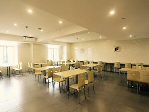 Une salle de conférence spacieuse, dotée de plusieurs tables et chaises, de grandes fenêtres et d’un sol carrelé.