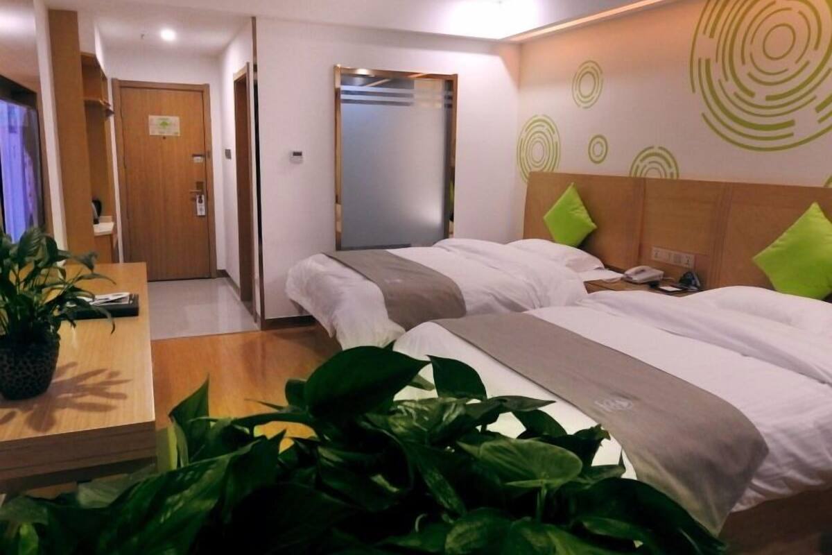 A hotel room with two beds, a desk, a mirror, and a potted plant.