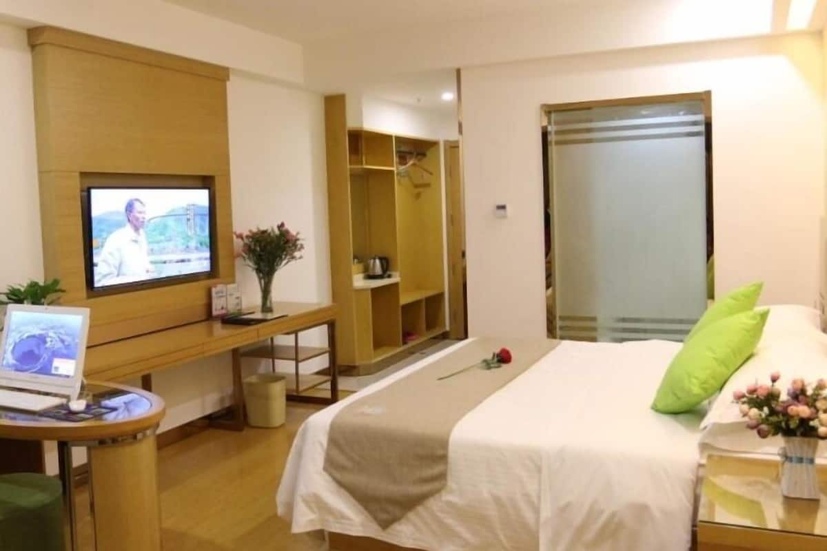 A hotel room with a bed, a desk with a computer, a TV, and a wardrobe.