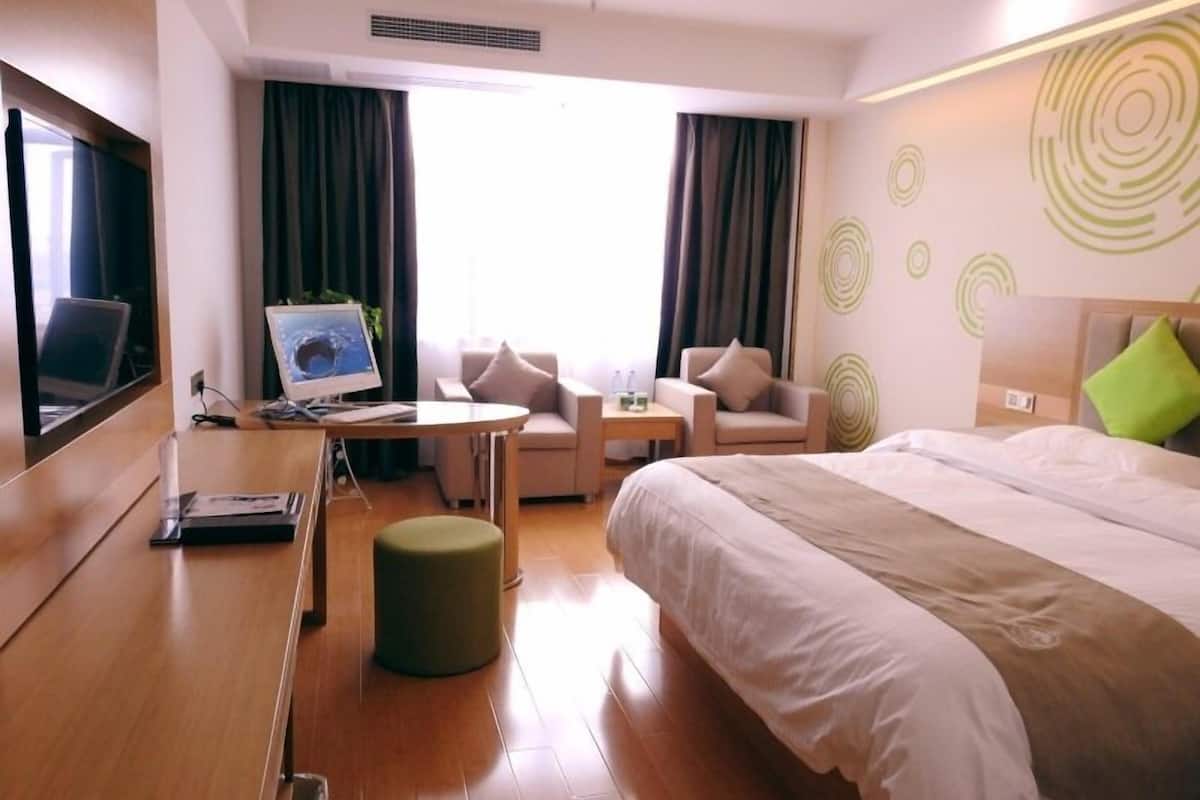 A hotel room with a bed, a desk with a laptop, a chair, a small table, and a window with curtains.