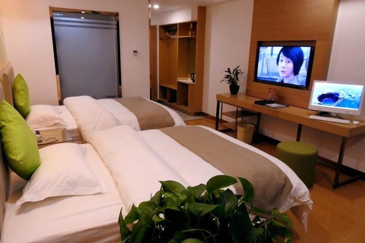 A hotel room with two beds, a desk with a computer, a television, and a potted plant.