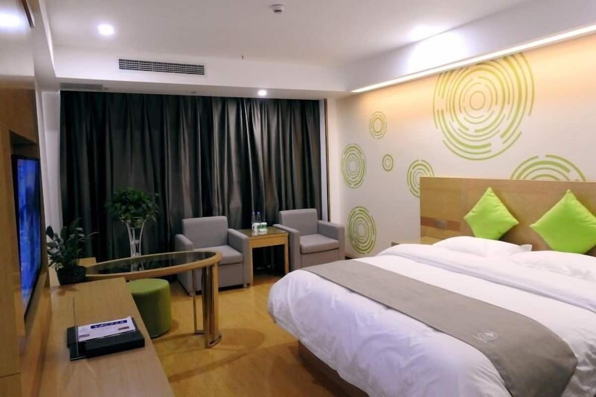 A hotel room with a bed, a desk, two chairs, a small table, and a TV.