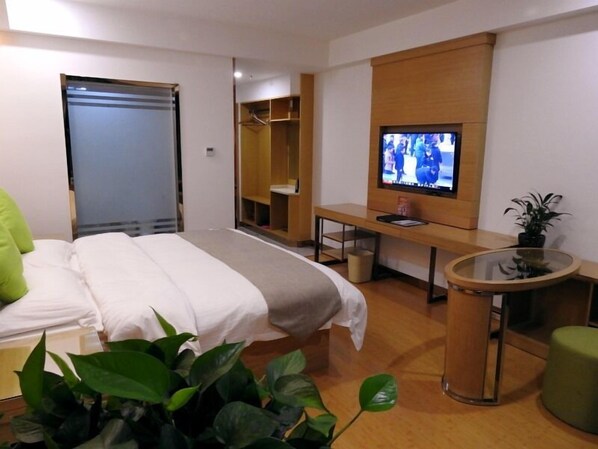 A hotel room with a bed, a desk, a TV, a mirror, and a small table with a plant. - GreenTree Inn HeFei Feidong New District Hui Shopping Mall Express Hotel (Hefei)