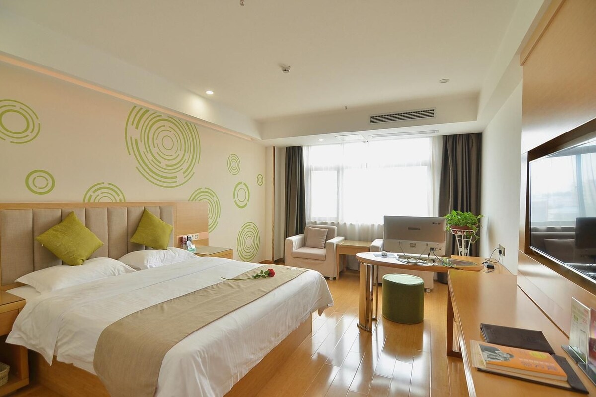 A hotel room with a large bed, a desk, a chair, a TV, and a window with curtains.