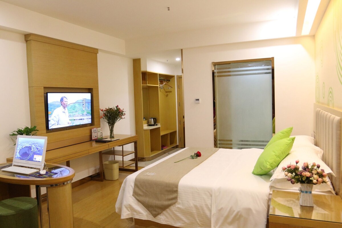 A hotel room with a bed, a desk with a laptop, a television, and a mirror.