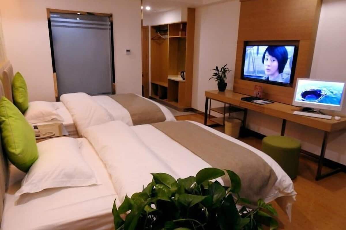 A hotel room with two beds, a desk with a computer, a television, and a plant.