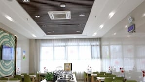 Een moderne eetruimte met een lange counter, groene stoelen en een wit plafond met ventilatie.