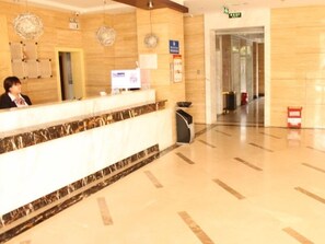 Un espace d’accueil d’hôtel avec un comptoir en marbre, un écran numérique et un réceptionniste.