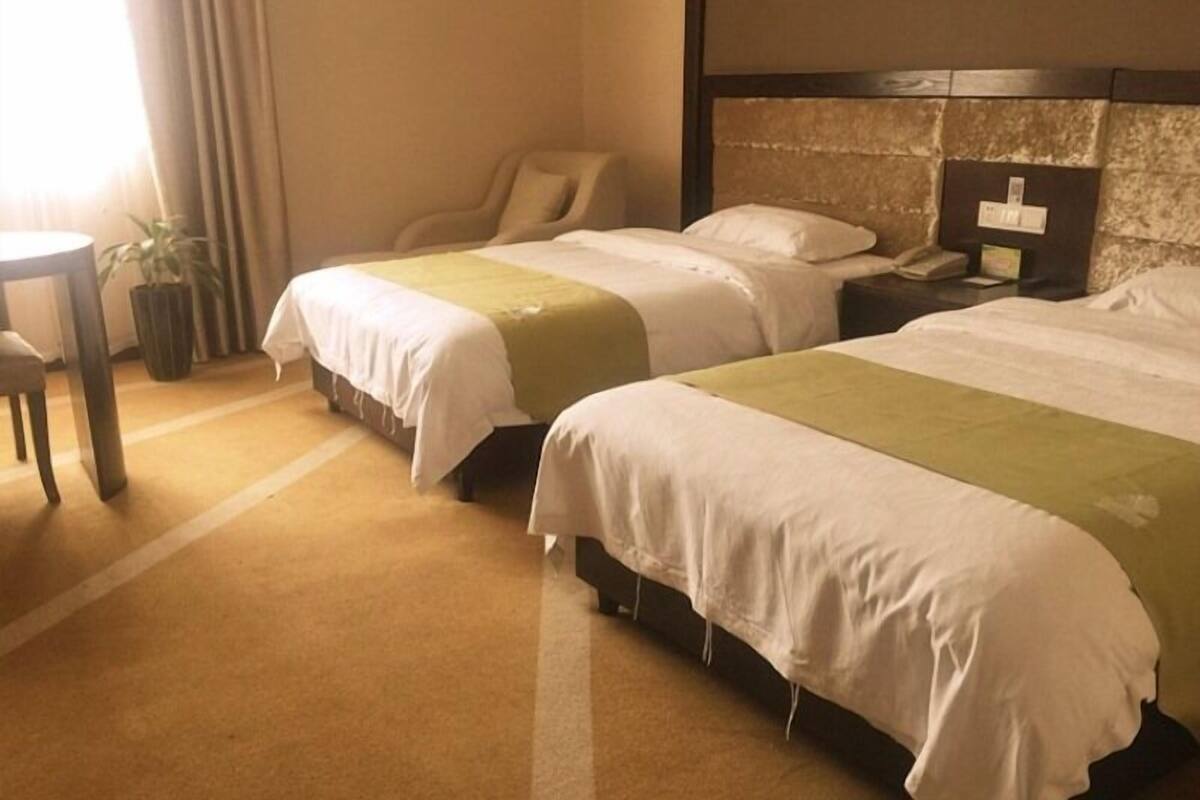 Une chambre d’hôtel avec deux lits, une chaise, une petite table et une plante en pot.