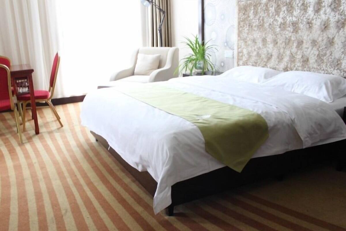 Une chambre d’hôtel avec un lit, une chaise, une petite table et une plante en pot.