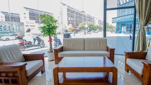 A modern hotel lobby with a sofa set, a coffee table, and a large window offering a view of the street and buildings outside. - GreenTree Inn Nantong Tongzhou Zhangzhishan Town Deli Square Express Hotel (Nantong)