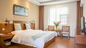Ein Hotelzimmer mit einem großen Bett, Nachttischen, einem Schreibtisch mit Stuhl, einem Fernseher und einem Fenster mit Vorhängen.