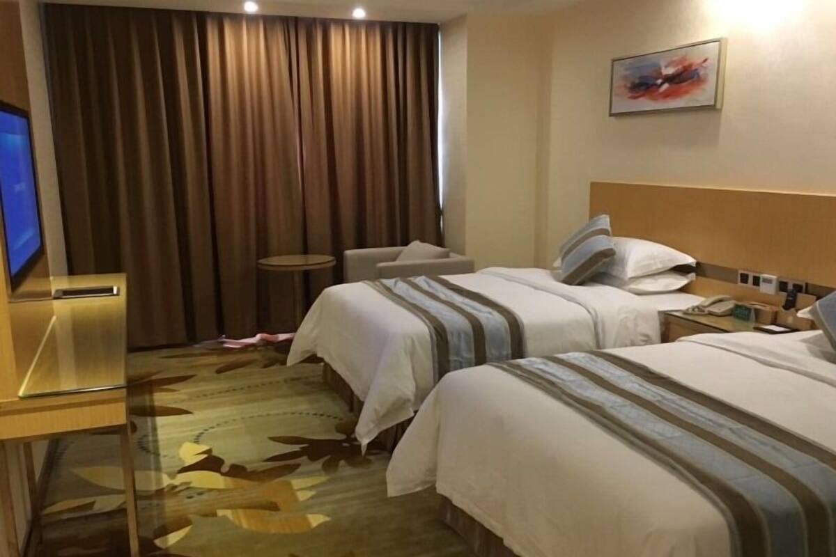 Ein Hotelzimmer mit zwei Betten, einem Schreibtisch, einem Stuhl, einem Fernseher und einem Gemälde an der Wand.