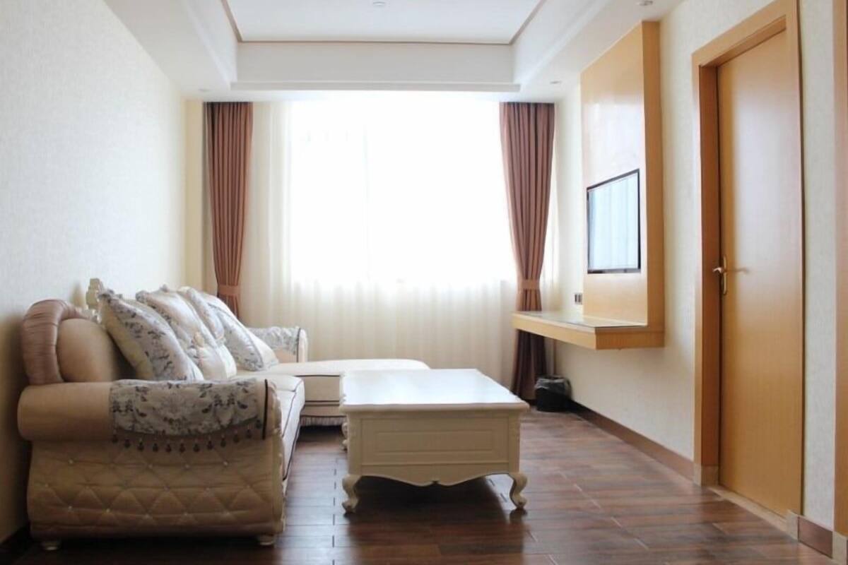 Ein Zimmer mit einer Couch, einem kleinen Tisch, einem Fenster mit Vorhängen und einer Tür.