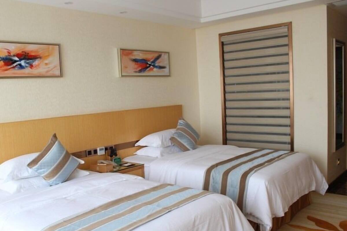 Ein Hotelzimmer mit zwei Betten, einem hölzernen Kopfteil, einem Streifenmuster-Vorhang und abstrakter Wandkunst.
