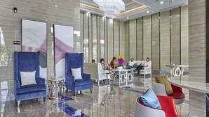 Un hall d’hôtel moderne avec un sol en marbre, des fauteuils bleus, un comptoir d’accueil et un lustre.