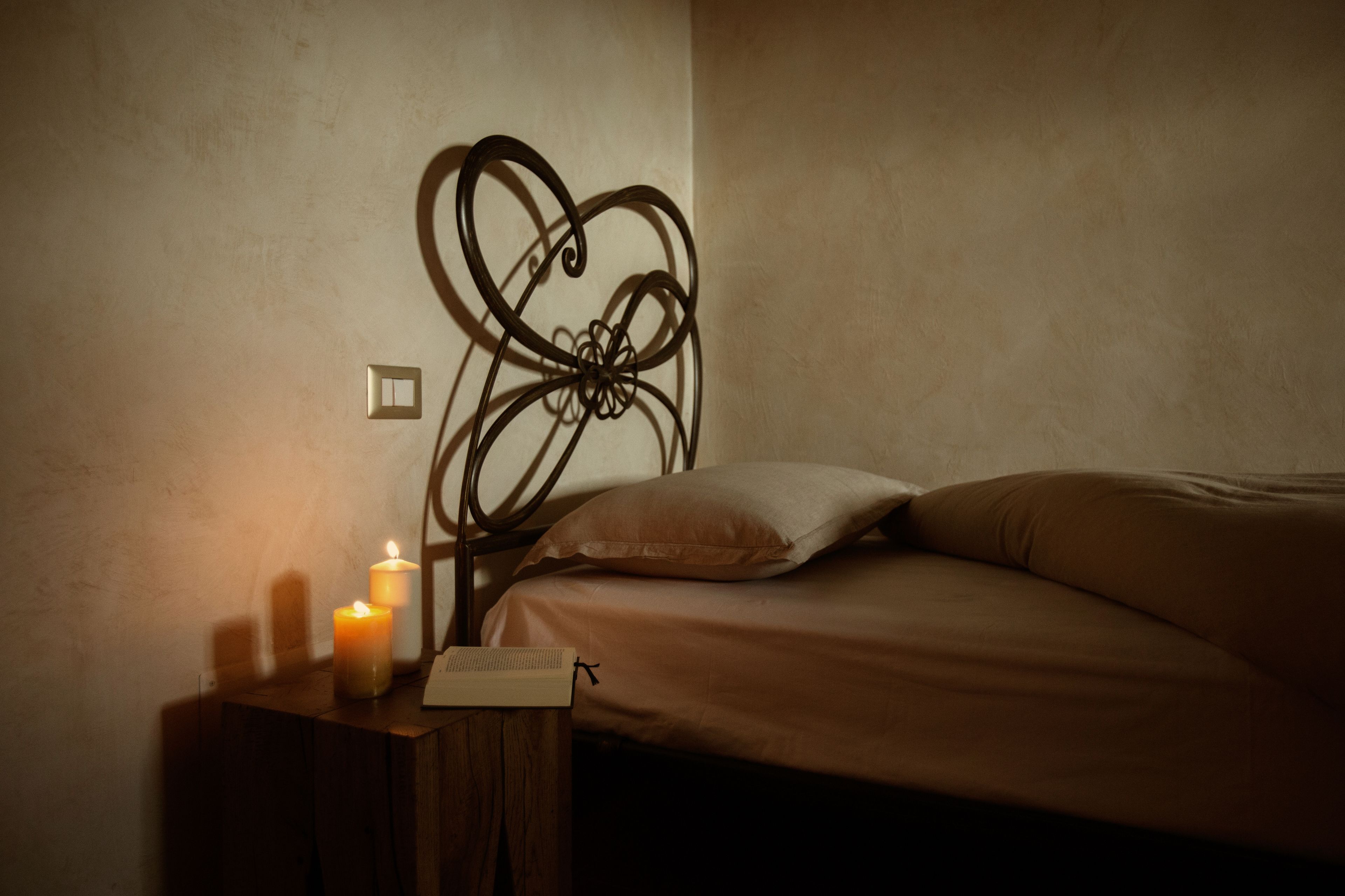 Un dormitorio con una cama, una mesita de noche con velas y un interruptor de luz en la pared.
