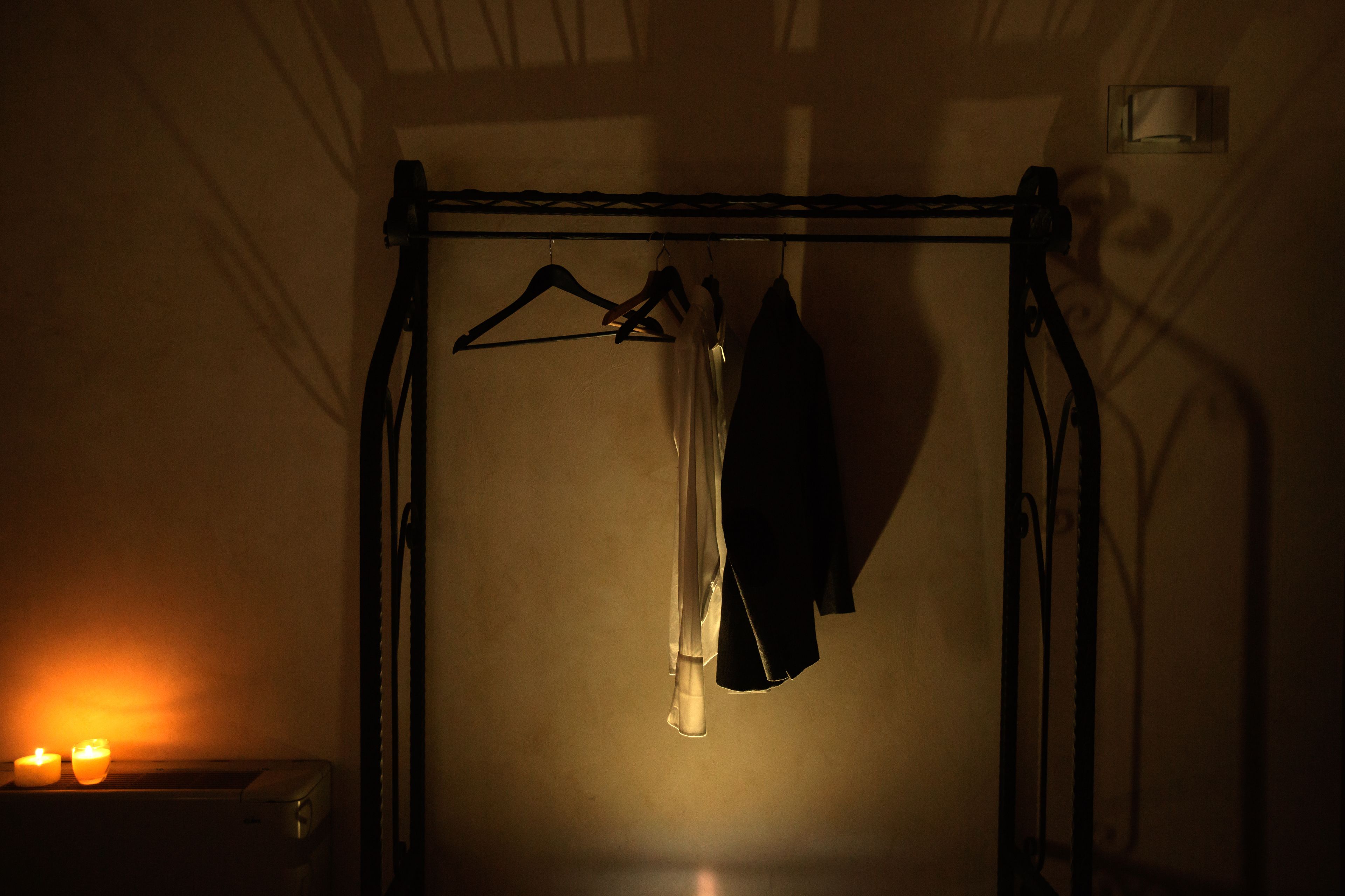 Une pièce faiblement éclairée, avec un portant à vêtements adossé au mur, une petite table ornée de bougies et une fenêtre donnant sur l’extérieur.