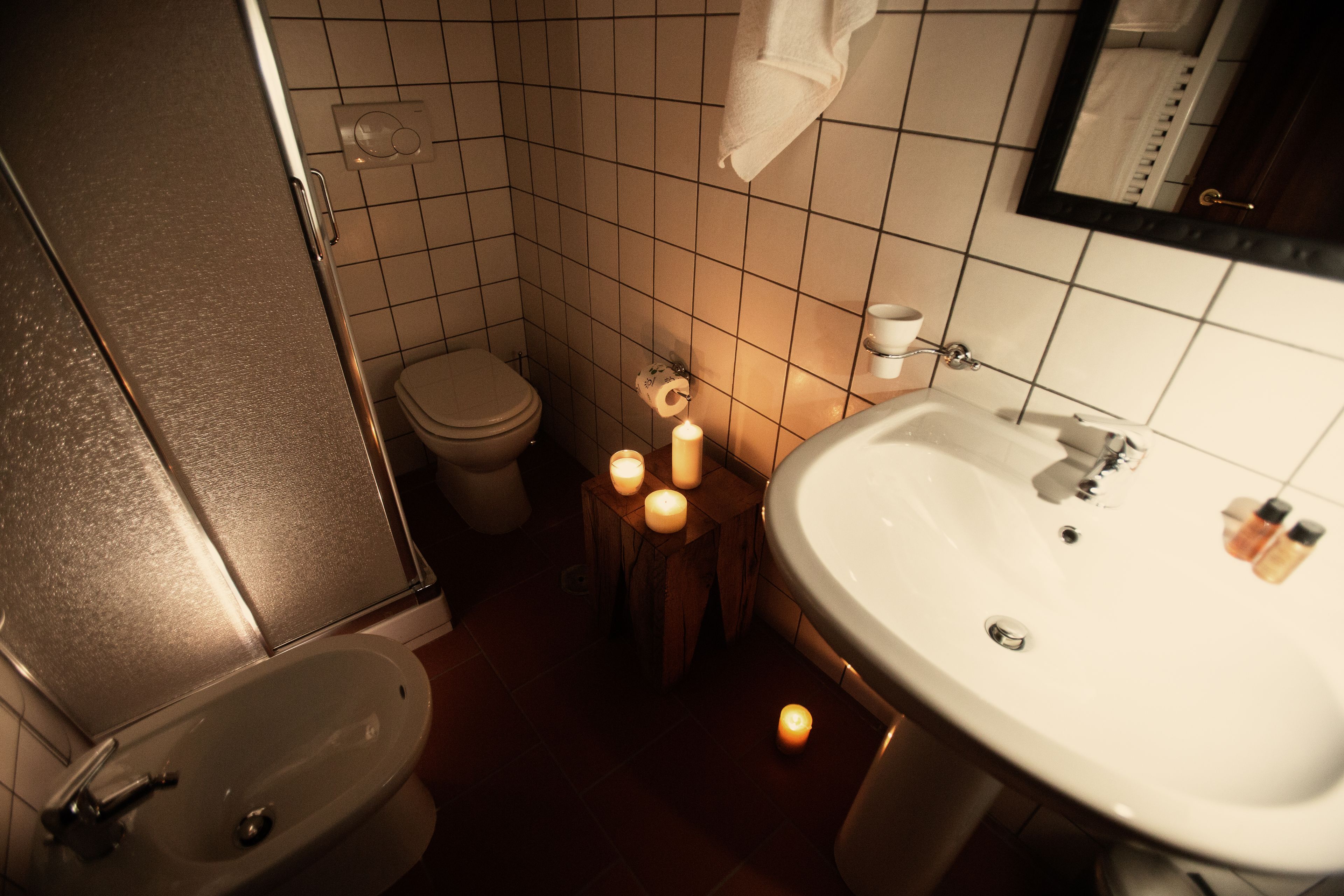 A bathroom with a sink, toilet, and mirror. There are candles on a wooden stool.