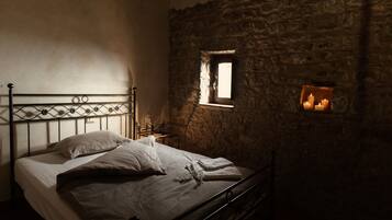 A bed in a room with stone walls, a small window, and a candle holder on the wall.