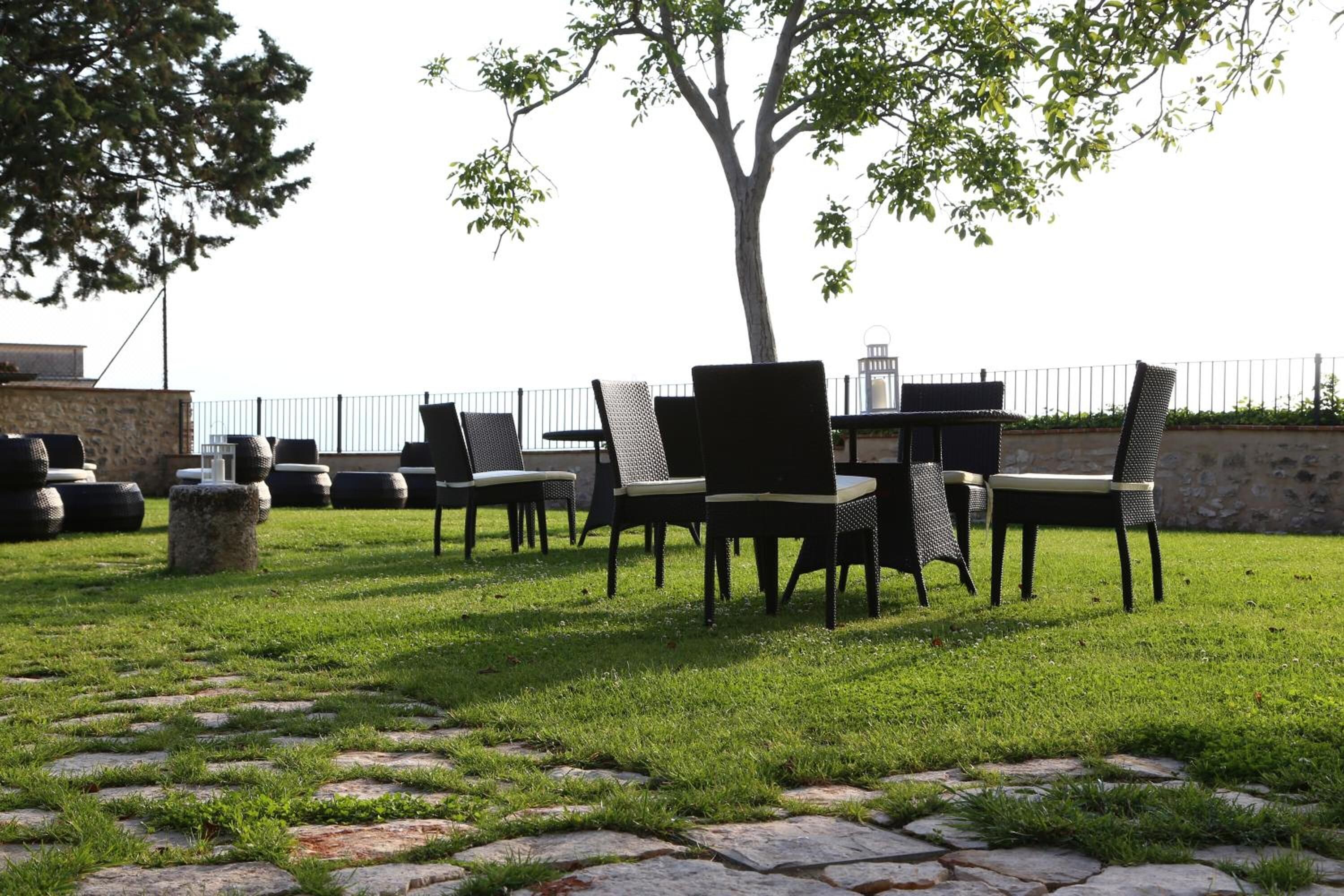 An outdoor seating area with chairs and tables, surrounded by stone paving and a tree.