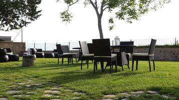 An outdoor seating area with chairs and tables, surrounded by stone paving and a tree.