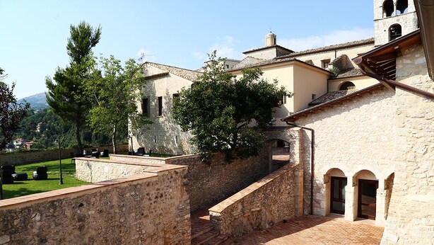 Un patio con muros de piedra, piso de ladrillo y un edificio con arcos.