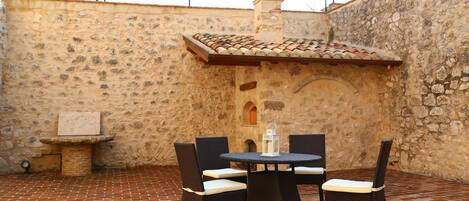 A patio with a stone wall, a tiled roof, and a table with chairs.