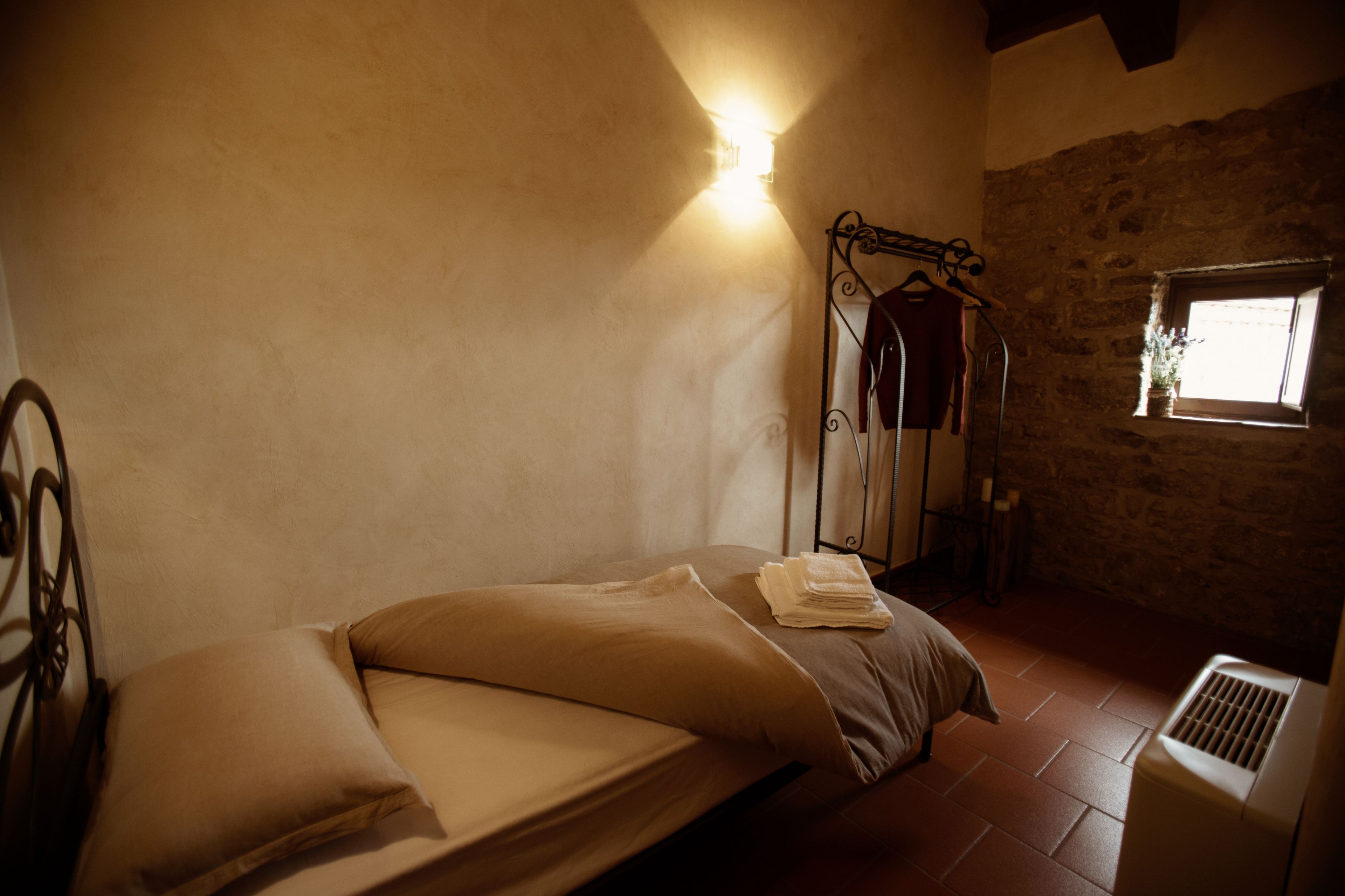 A single bed with a metal frame, a wall-mounted light, and a window with a view of the outside.