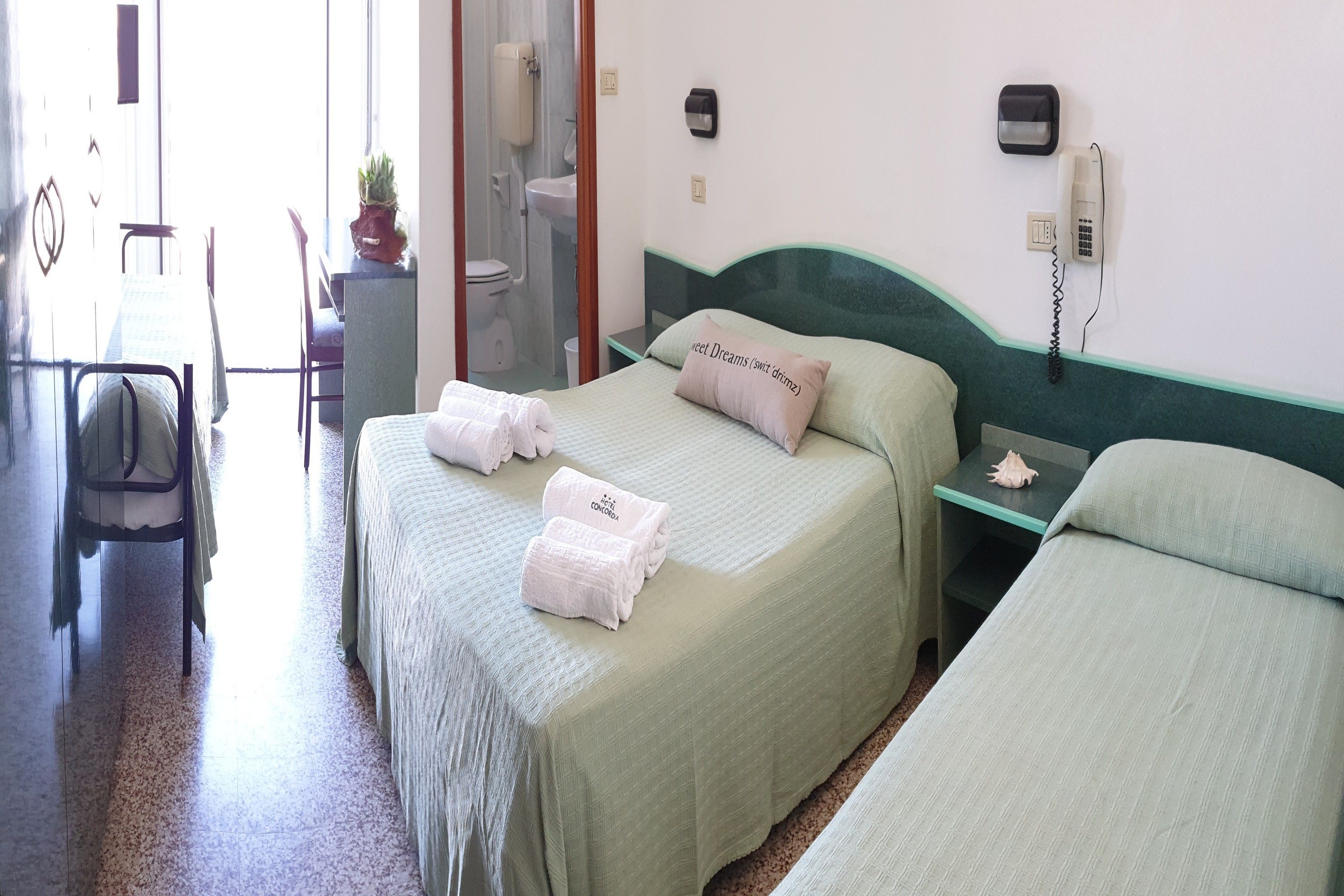 A hotel room with two beds, a desk, a chair, a telephone, and a mirror.