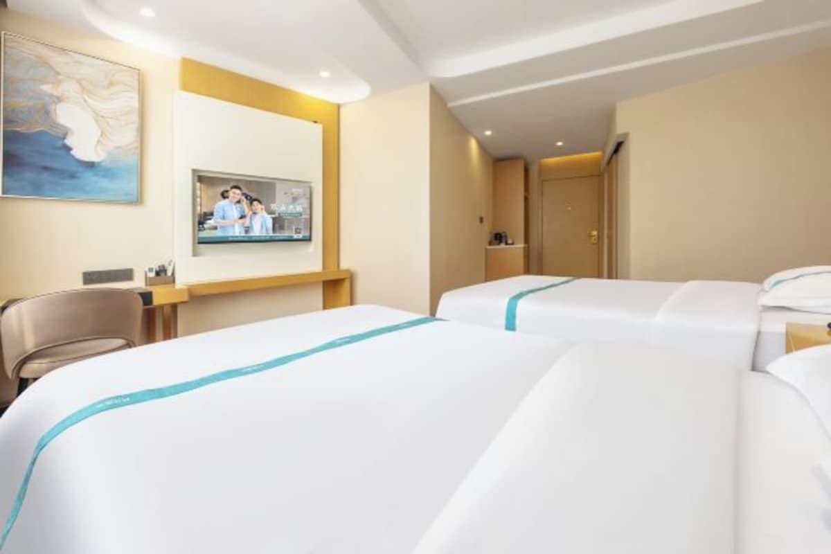 A hotel room with two beds, a desk, a television, and a painting on the wall.