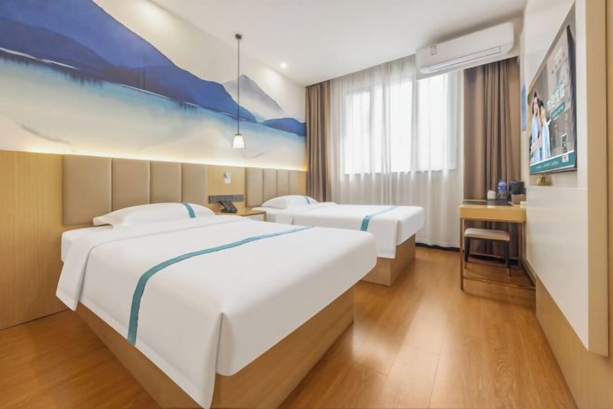 Habitación de hotel con dos camas, un escritorio y un ventanal grande con cortinas.