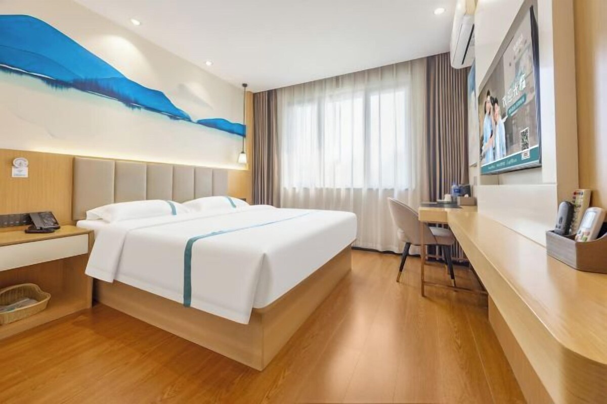 Habitación de hotel con cama, escritorio, silla, lámpara de escritorio, teléfono y aire acondicionado instalado en la pared.