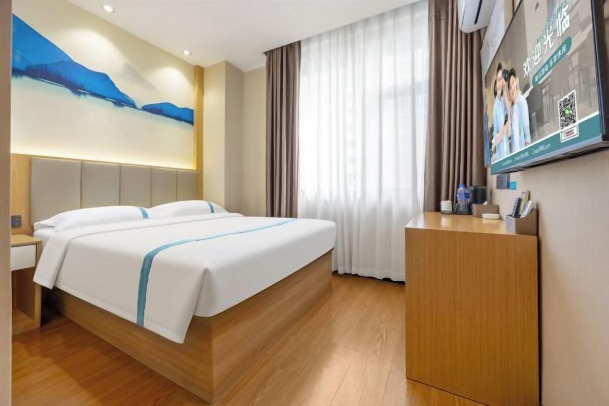 Habitación de hotel con una cama grande, cabecera de madera, escritorio con silla, televisor y un cuadro en la pared.
