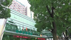 A modern building with a glass facade, flags, and a sign indicating a hotel. - GreenTree Inn Huzhou Wuxing District South Street Chaoyin Bridge Business Hotel (Huzhou)