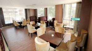 A hotel lobby with a central dining table surrounded by chairs, a sofa, and a large window with curtains. - GreenTree Inn Huzhou Wuxing District South Street Chaoyin Bridge Business Hotel (Huzhou)