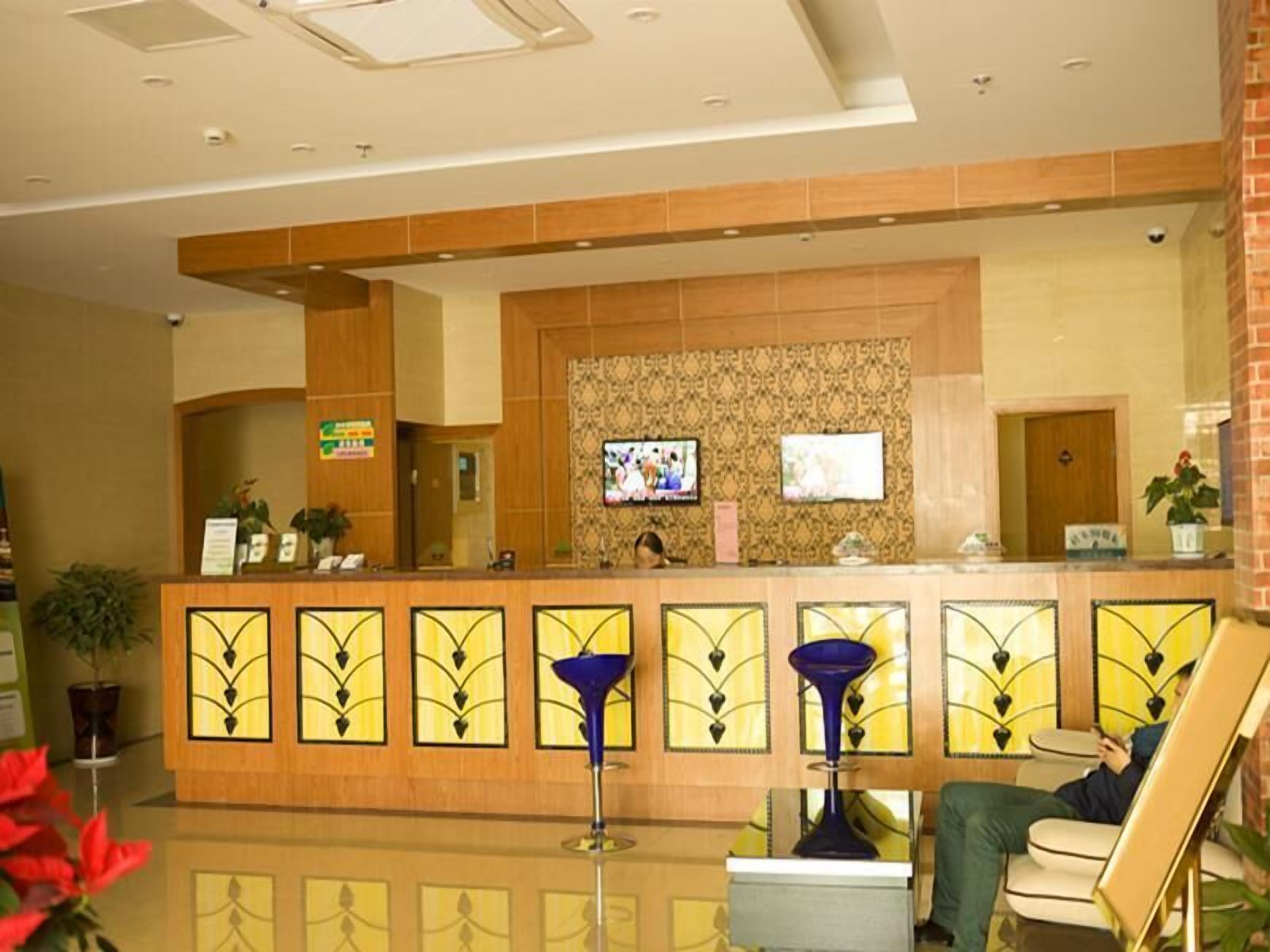 Zona de recepción de hotel con mostrador, televisor y área de descanso.
