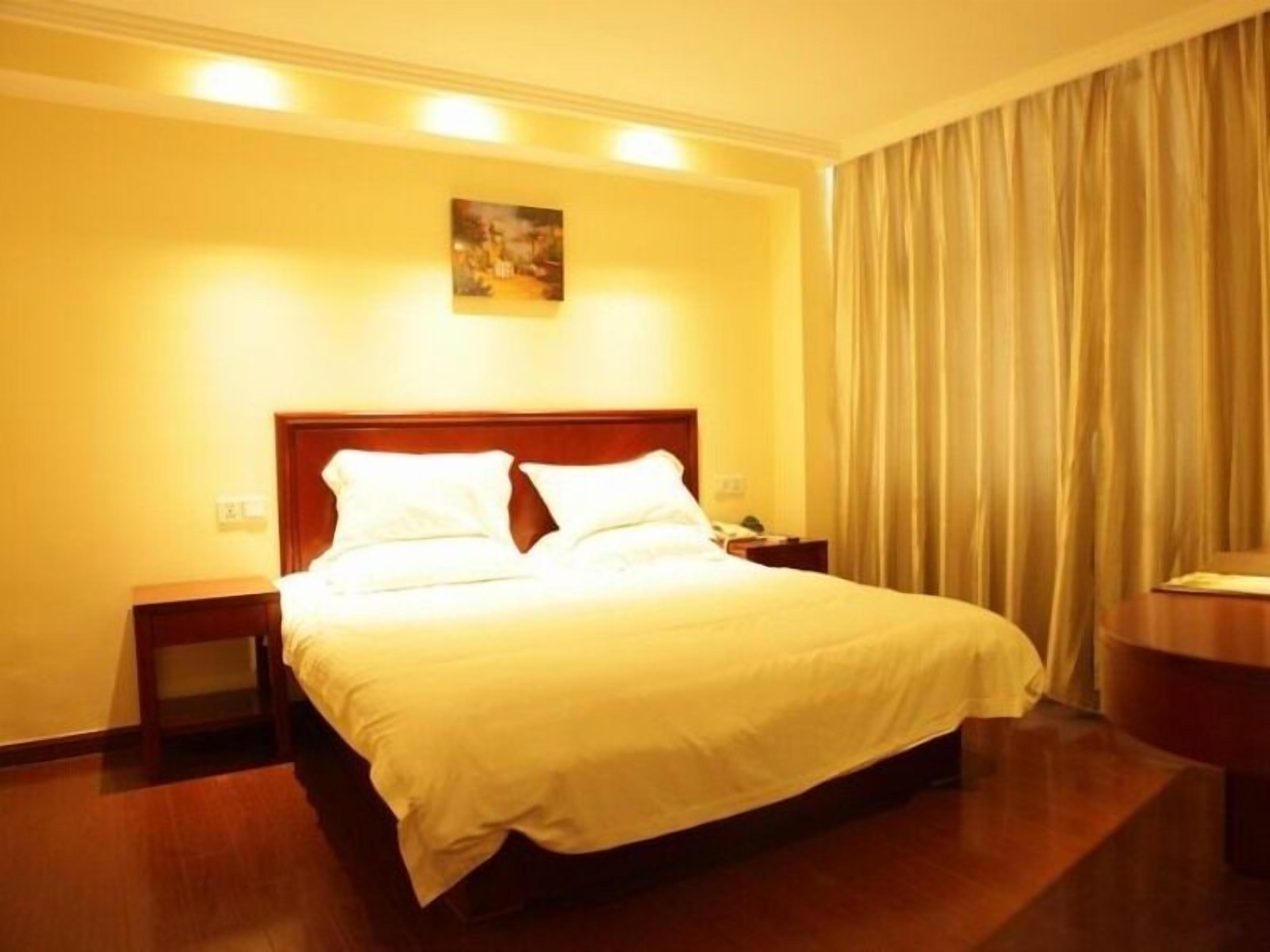 Une chambre d’hôtel avec un grand lit, deux tables de chevet, une commode, un tableau au mur et un rideau à la fenêtre.