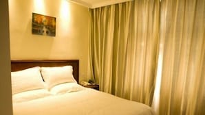 Ett hotellrum med en stor säng, ett nattduksbord, en telefon och gröna gardiner.