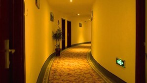 En hotellkorridor med ett heltäckningsmatta på golvet, dörrar och en krukväxt.