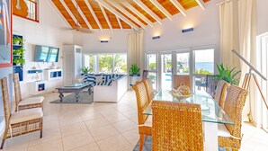 A spacious living area with a glass dining table, wicker chairs, and a modern sofa. - Villa North Winds Orange Hill (Nassau)