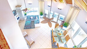 A spacious living area with a high ceiling, large windows, and a dining area with wicker furniture. - Villa North Winds Orange Hill (Nassau)