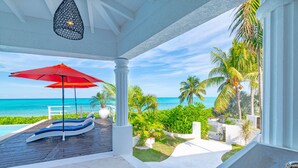 A covered outdoor area with a pool, lounge chairs, and a red umbrella. - Villa North Winds Orange Hill (Nassau)