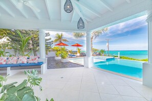 A poolside area with a view of the ocean, a seating area with cushions, and two red umbrellas.
