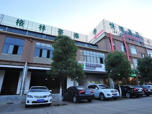 Un hôtel à étages, un parking avec plusieurs voitures et des panneaux indiquant les différents services proposés.