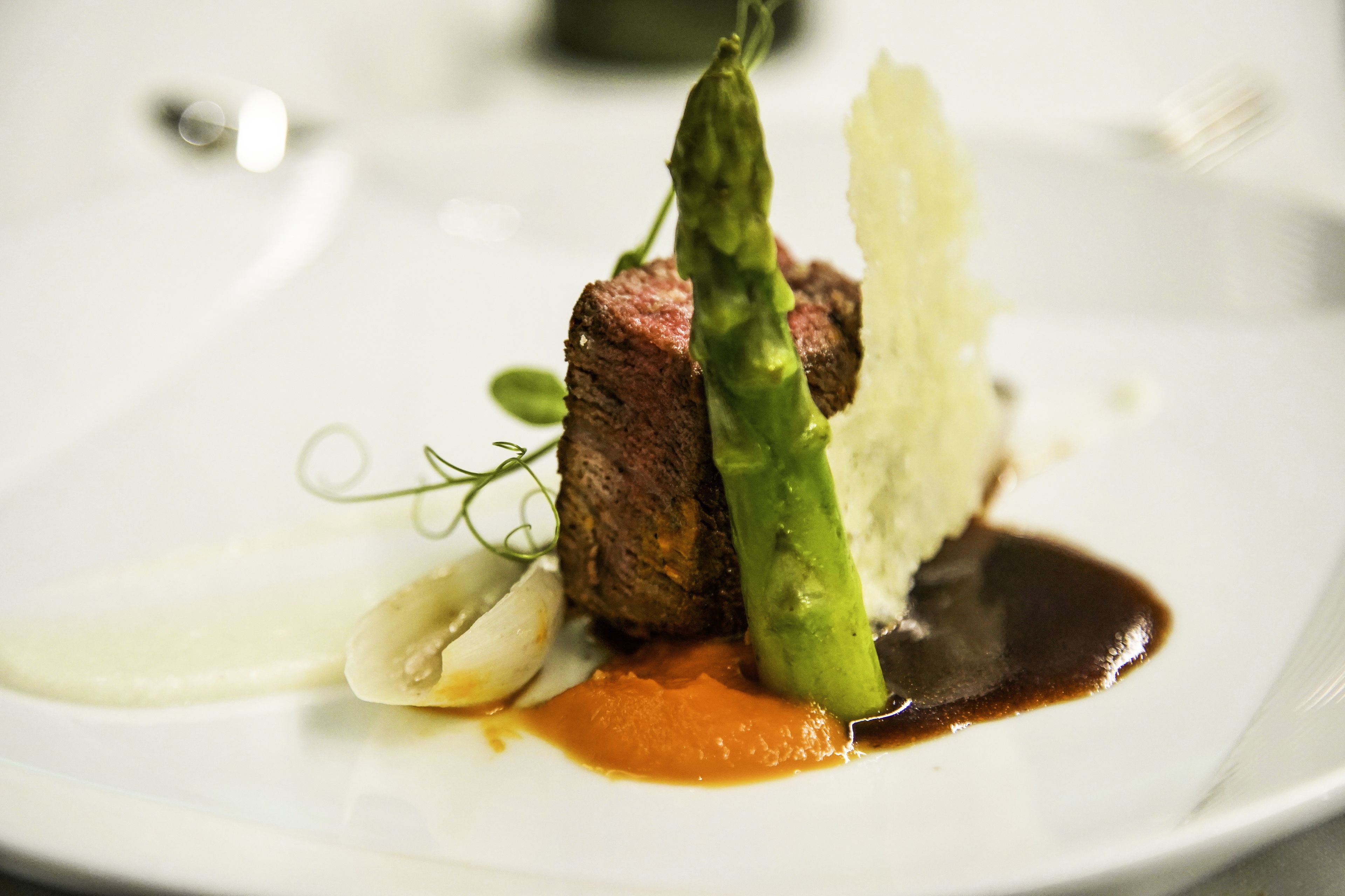 A plate with a piece of meat, asparagus, and a sauce.