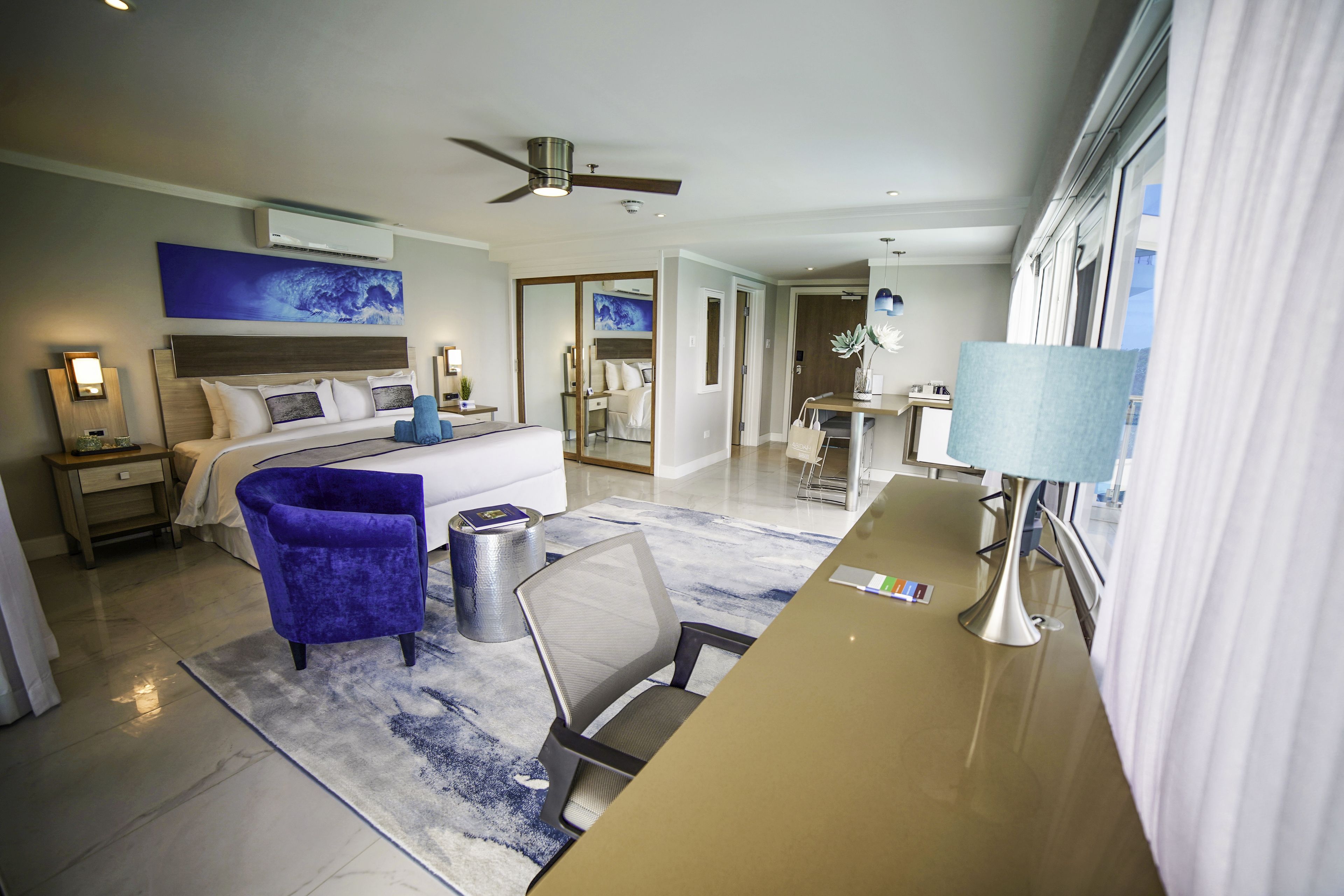 A modern hotel room with a bed, a desk, a chair, and a ceiling fan.
