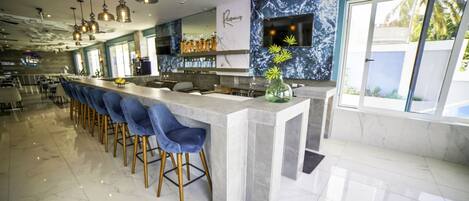 Un espace bar moderne avec des comptoirs en marbre, des tabourets de bar bleus et des luminaires suspendus.